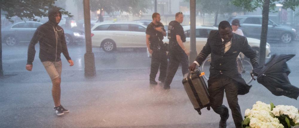 Passanten und ein Portier rennen am Dienstag in Berlin vor dem Adlon Hotel durch den heftigen Regen. 