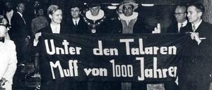 Zwei junge Männer tragen ein Plakat mit der Aufschrift "Unter den Talaren Muff von 1000 Jahren", dahinter gehen zwei Männer in akademischen Roben.