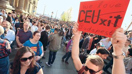 Ein Mann hält bei einer Demonstration ein Plakat mit der Aufschrift "CEUxit" hoch. Der Schriftzug ist durchgestrichen und durch die Worte "We love Budapest" ergänzt.