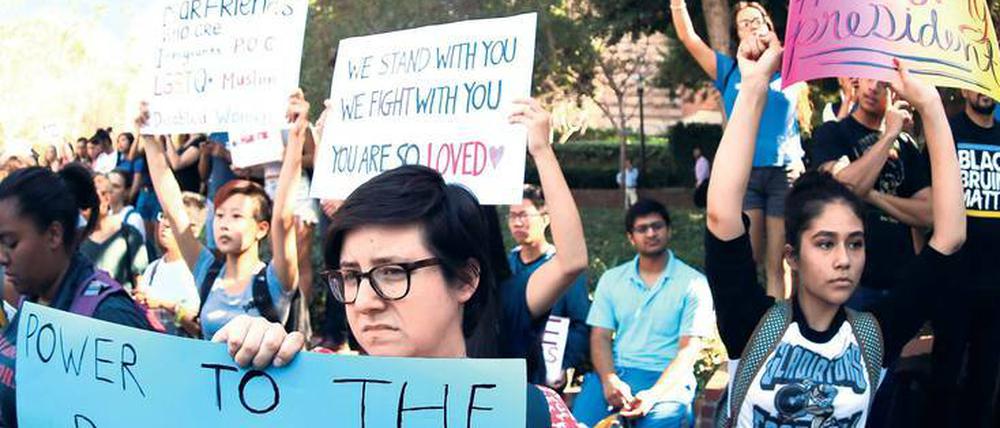 Studierende stehen auf einem Campus und halten Schilder mit Parolen doch, unter anderem ist "Not my President" zu lesen.