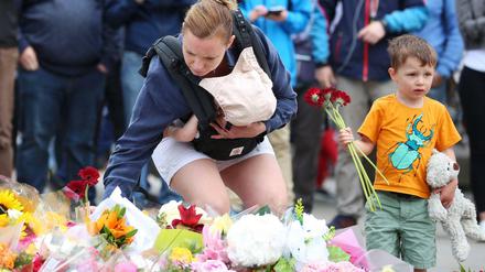 Eine Mutter mit einem Baby im Arm legt an der London Bridge Blumen nieder.