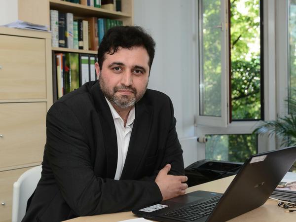 Ein Mann sitzt an einem Laptop am Schreibtisch und blickt in die Kamera.