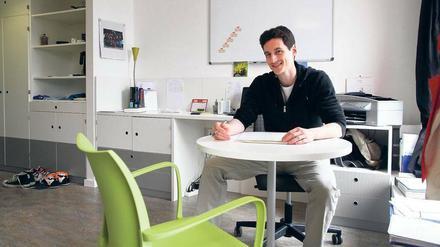 Ein junger Mann sitzt in einem modern eingerichteten Appartement an einem Tisch.