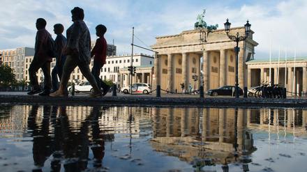 Passanten gehen nach einem kurzen, aber heftigen Regenschauer am Brandenburger Tor vorbei.