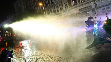 Ein Mann klammert sich im Schanzenviertel an einen Räumpanzer - die Polizei geht mit einem Wasserwerfer gegen ihn vor.