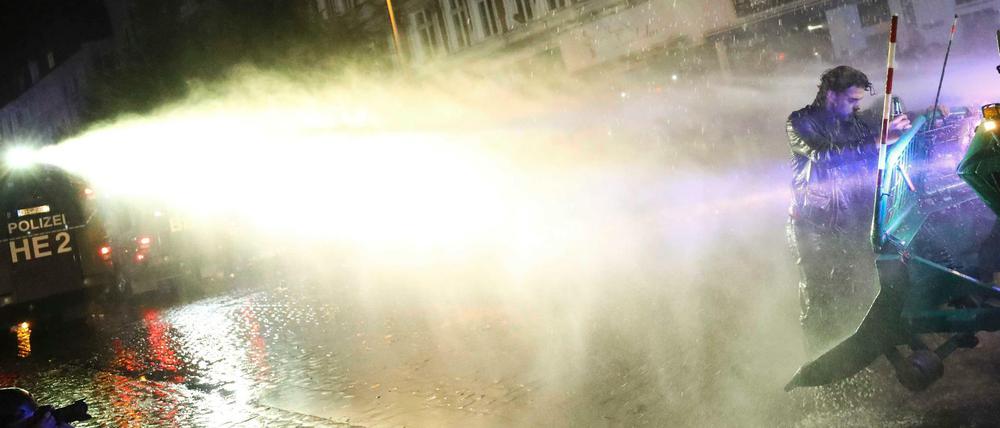 Ein Mann klammert sich im Schanzenviertel an einen Räumpanzer - die Polizei geht mit einem Wasserwerfer gegen ihn vor.