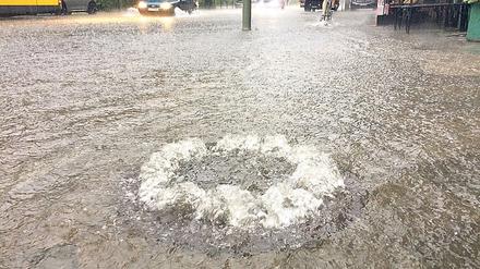 Wasser sprudelt Ende Juni in Berlin auf einer überfluteten Straße im Stadtteil Schöneberg aus einem Gully.