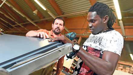 Asylbewerber Omar Ceesay (r) arbeitet in der Schreinerei Holitsch in Tettnang-Hiltensweiler (Baden-Württemberg) an einer Tür.