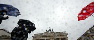Bei Regen gehen Touristen vor dem Brandenburger Tor in Berlin vorbei. 