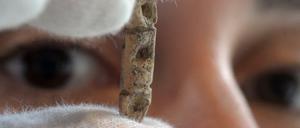 Eine Frau betrachtet eine Perle, die sie zwischen den Fingern hält.