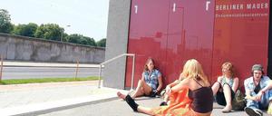 Schülerinnen und Schüler sitzen vor der Tür einer Mauergedenkstätte in Berlin.