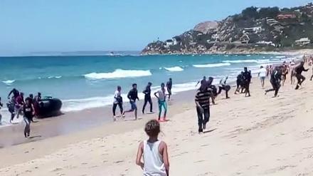 Eine Frau beobachtet wie Flüchtlinge mit einem Schlauchboot am Strand von Cadíz ankommen.