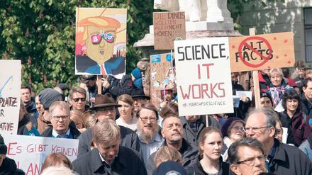 Demonstranten stehen vor einem Universitätsgebäude und halten Schilder hoch mit Aufschriften wie "Science, it works".