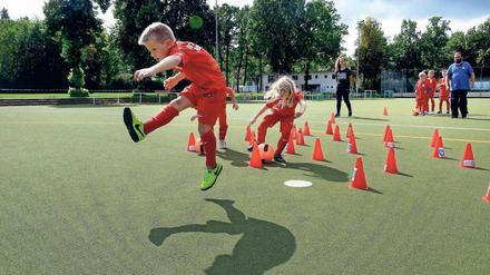 Jungen und Mädchen spielen Fußball beim Feriencamp in Lichterfelde. Im Hintergrund Trainerin Vicdan Yavas und Trainer Alexander Regh. 