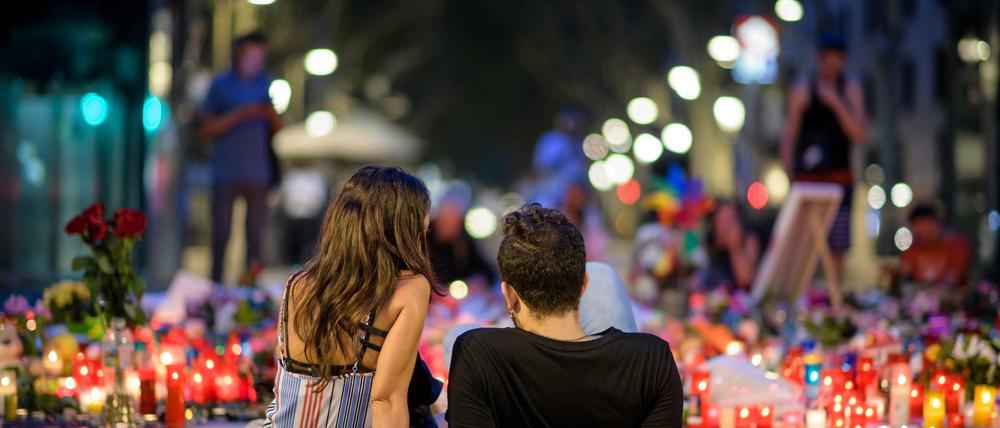 Ein Pärchen sitzt am 19.08.2017 in den frühen Morgenstunden vor niedergelegten Rosen und Kerzen auf der Flaniermeile Las Ramblas in Barcelona.