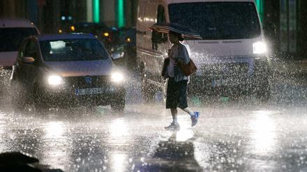 Eine Frau hält einen Regenschirm und läuft am Freitagabend in Berlin bei starkem Regenfall über eine Kreuzung.