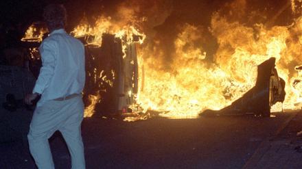  Ein Mann steht 27.08.1992 vor einem brennenden Pkw auf einer Straße am zentralen Asylbewerberheim von Mecklenburg-Vorpommern in Rostock-Lichtenhagen. 