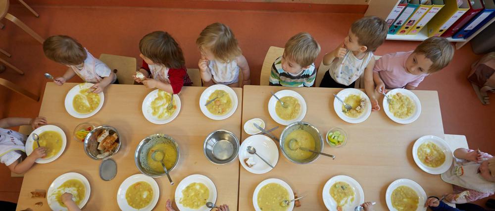 Kita-Kinder sitzen an einem Tisch und essen Suppe.