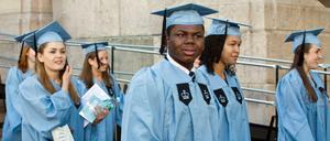 Studierende in Talaren gehen über einen Campus.