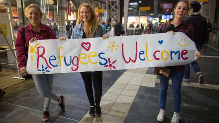 Die Stimmung in Deutschland vor zwei Jahren: Drei junge Frauen stehen in Frankfurt am Main im Hauptbahnhof mit einem Begrüßungsplakat.