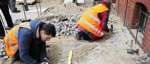 Steinsetzer bei der Arbeit in der Pappelallee, deren ursprünglicher Gehweg nach Straßenbauarbeiten wiederhergestellt wurde.