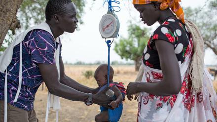Ein Mitarbeiter einer Hilfsorganisation wiegt im Südsudan ein Kind.