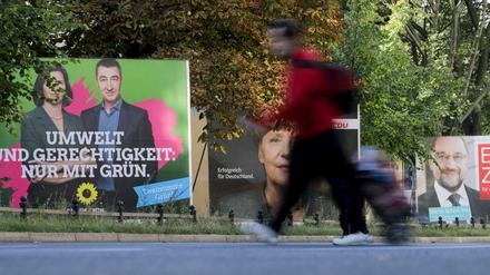 Ein Passant geht am 18.09.2017 in Berlin an Wahlplakaten mit dem Porträt der Grünen-Spitzenkandidaten Katrin Göring-Eckardt und Cem Özdemir, Bundeskanzlerin Merkel (CDU) und dem SPD-Parteivorsitzenden Martin Schulz vorbei. 