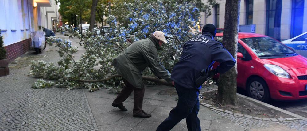 Ein Polizist und ein Anwohner beseitigen am 05.10.2017 in der Gieselerstraße in Berlin Sturmschäden.
