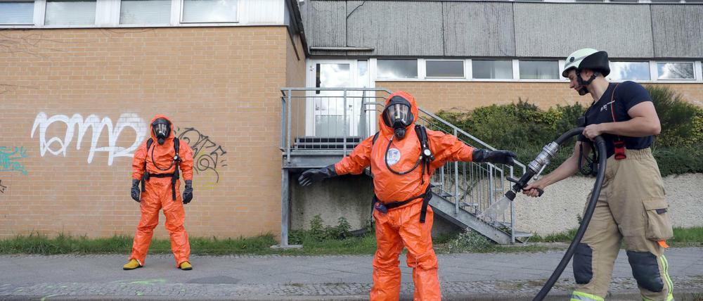 Einsatzkräfte der Feuerwehr werden nach ihrem Einsatz im Rahmen des Chlorgas-Austritts in einer Schwimmhalle in Berlin-Buch mit Wasser abgespritzt. 