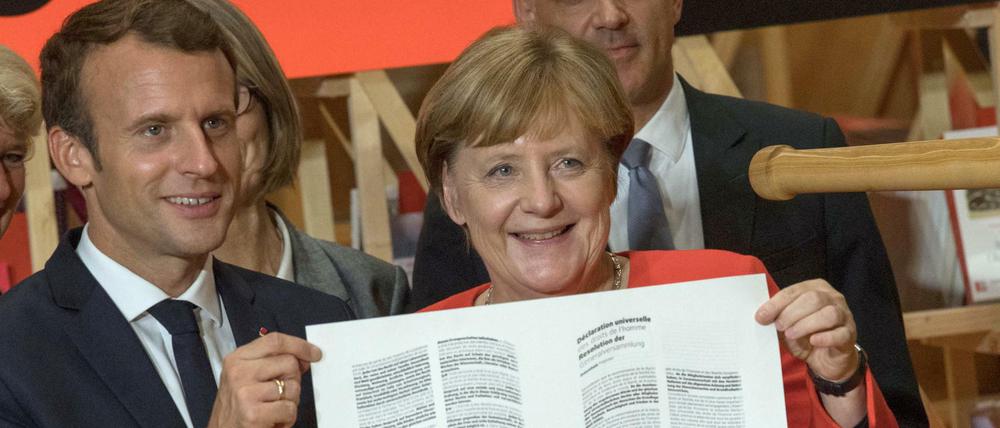 Kanzlerin Merkel und Frankreichs Präsident Macron halten auf der Buchmesse die Erklärung der Menschenrechte.