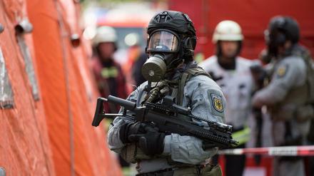 Nur Übung: Schwerbewaffnete Polizisten mit Atemschutzmasken stehen zusammen mit Feuerwehrleuten vor einem Dekontaminationszelt.