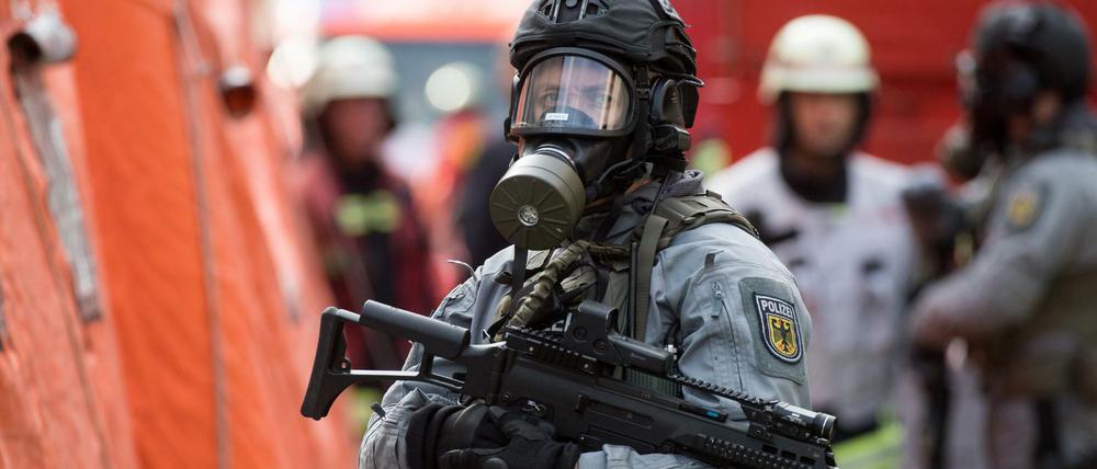 Nur Übung: Schwerbewaffnete Polizisten mit Atemschutzmasken stehen zusammen mit Feuerwehrleuten vor einem Dekontaminationszelt.