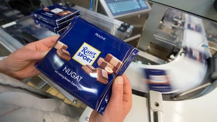 Eine Mitarbeiterin des Schokoladenherstellers Ritter Sport prüft die Verpackung einer Tafel Schokolade.