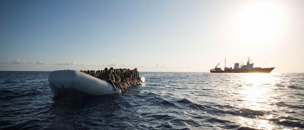 Ein Flüchtlingsboot auf dem Mittelmeer und im Hintergrund ein Schiff der Hilfsorganisation SOS Mediterranee.