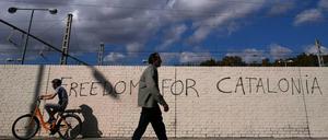 Menschen passieren in Barcelona eine Mauer mit dem Schriftzug "Freiheit für Katalonien".