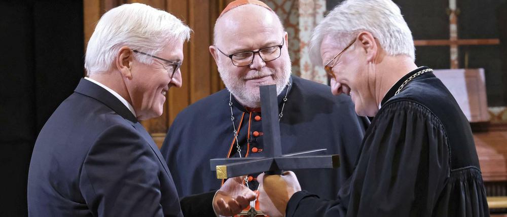 Landesbischof Bedford-Strohm (r.) und Kardinal Marx überreichen ein Kreuz an Bundespräsident Steinmeier (l.)