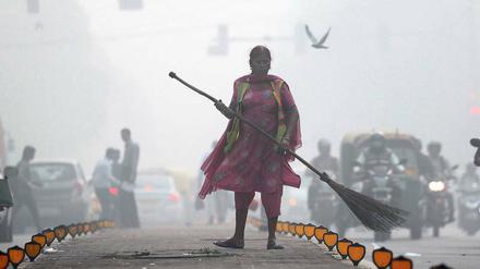 Eine Straßenkehrerin arbeitet im Smog von Delhi.