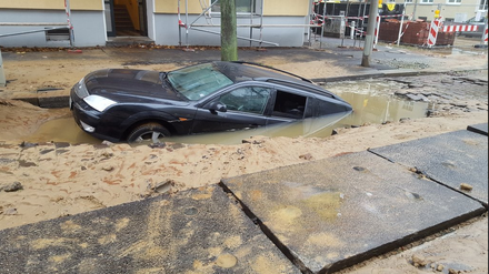 Ein Auto versinkt in der unterspülten Straße.