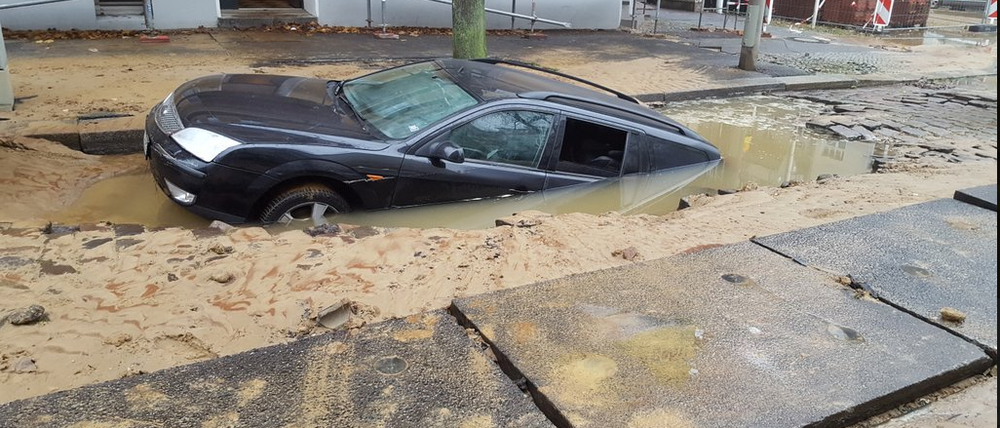 Ein Auto versinkt in der unterspülten Straße.
