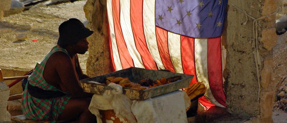 Eine Frau verkauft im Mai 2010 in Port-au-Prince, Haiti, gebackene Bananen und sitzt neben einer US-Nationalflagge.
