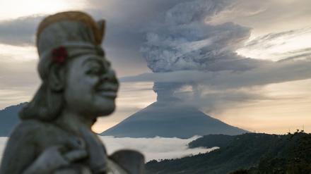 Eine Statue ist neben der riesigen Rauchsäule über dem Vulkan Mount Agung zu sehen.