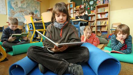 Schüler arbeiten im Klassenraum am Tisch, andere sitzen lesend auf Isomatten.