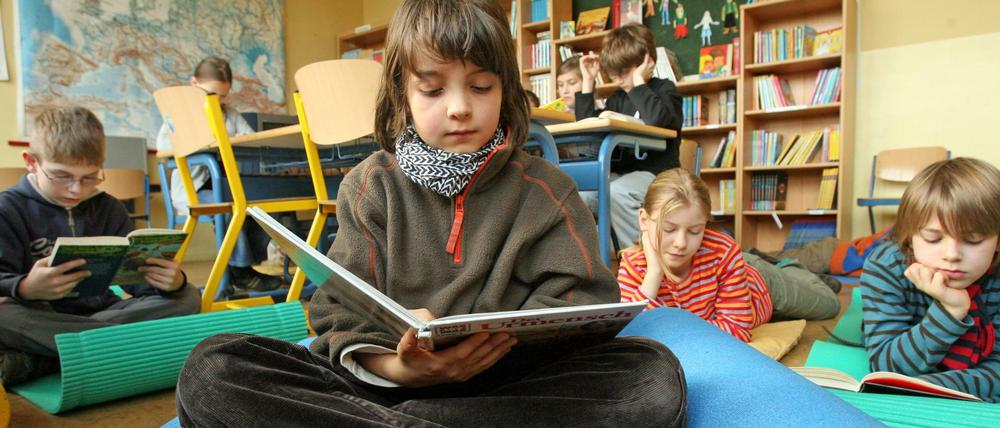 Schüler arbeiten im Klassenraum am Tisch, andere sitzen lesend auf Isomatten.
