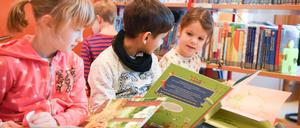 Kinder sitzen in einer Bibliothek und lesen in Bilderbüchern.