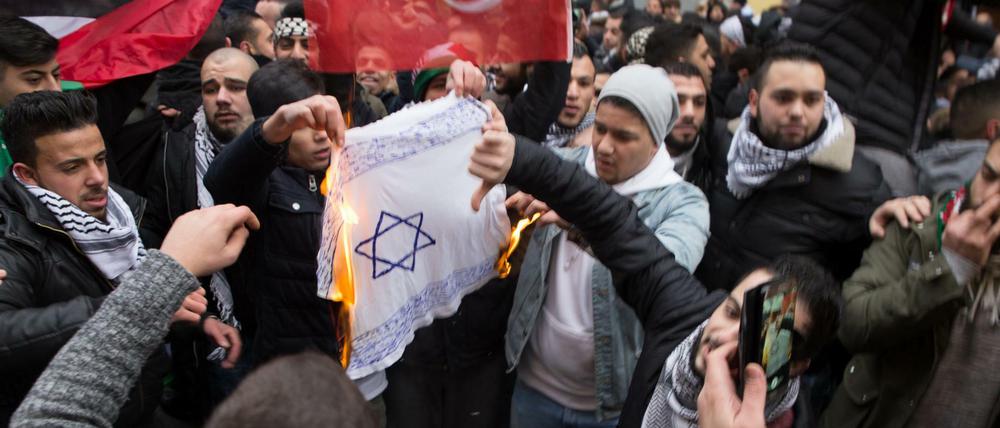 Teilnehmer einer Demonstration verbrennen am 10.12.2017 eine selbstgemalte Fahne mit einem Davidstern in Berlin im Stadtteil Neukölln. Die geplante Verlegung der US-Botschaft in Israel von Tel Aviv nach Jerusalem sorgte auch in Berlin für Proteste. Bei den pro-palästinensischen Demonstrationen wurden Fahnen mit dem Davidstern angezündet.