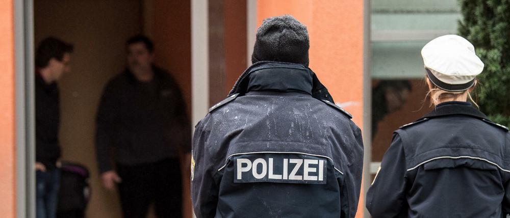 Zwei Polizisten stehen vor dem Mehrfamilienhaus, in dem die Polizei in der Nacht zum Montag einen mit Messern bewaffneten Familienvater erschossen hat. 
