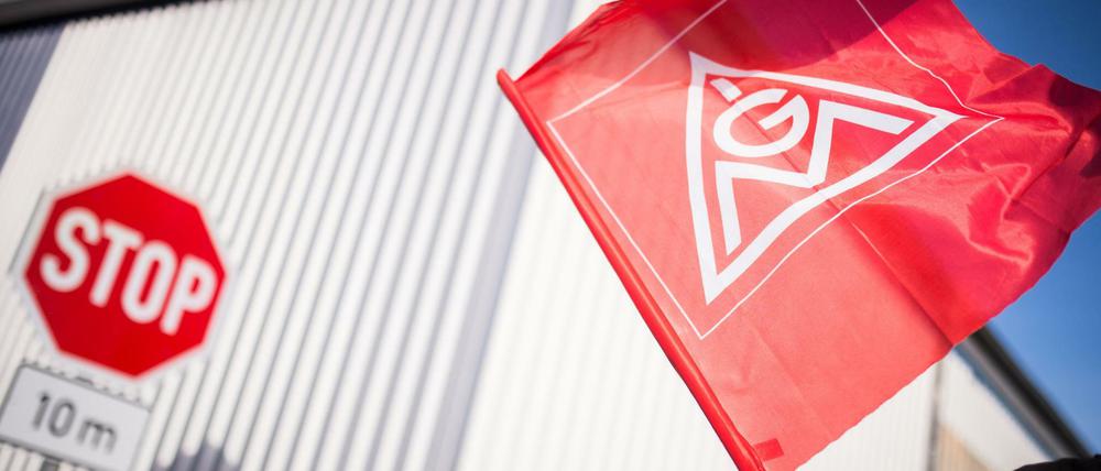 Ein streikender Mitarbeiter hält eine Fahne der IG Metall in die Höhe.