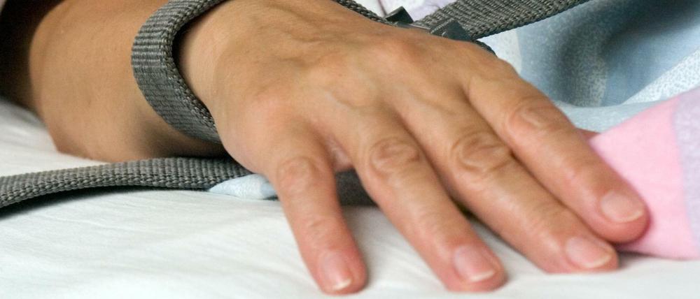 Eine Patientin in der Krankenpflege ist mit einem Textilband an der Hand festgebunden. 