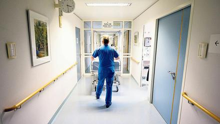 Ein Krankenpfleger schiebt in einer Berliner Klinik ein Krankenbett durch den Flur.