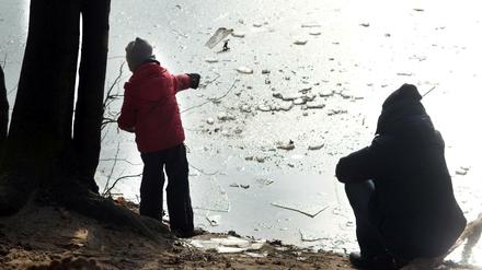 Winter in Berlin. Die Seen frieren langsam zu, sind aber noch nicht sicher. Am Schlachtensee Vater und Sohn werfen Eis auf die Eisfläche. 
